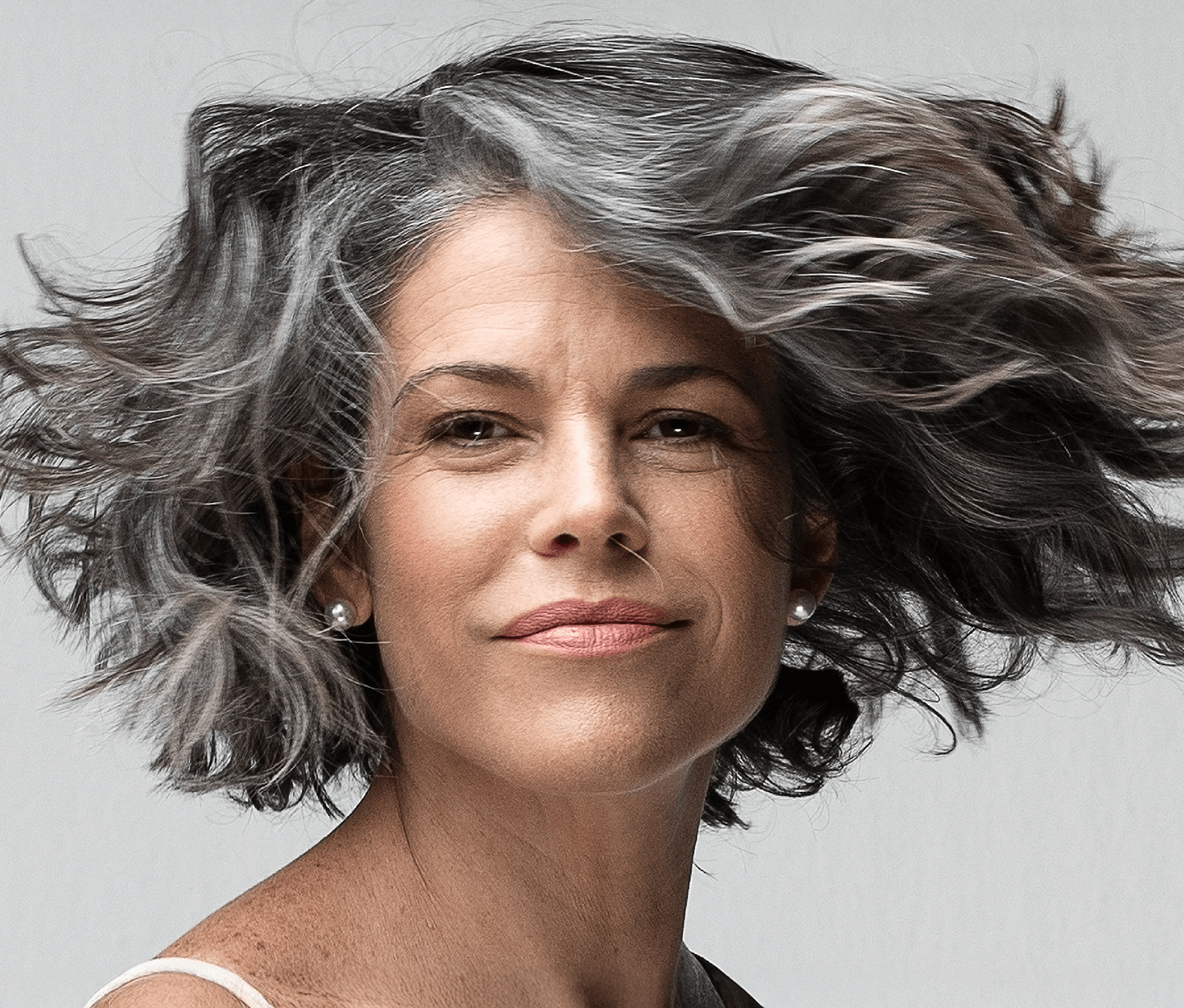 Woman with gray hair blowing in the wind against a neutral background