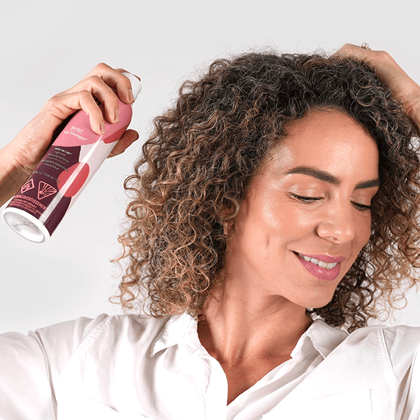 Woman with curly hair holding a bottle of hair product against a light background